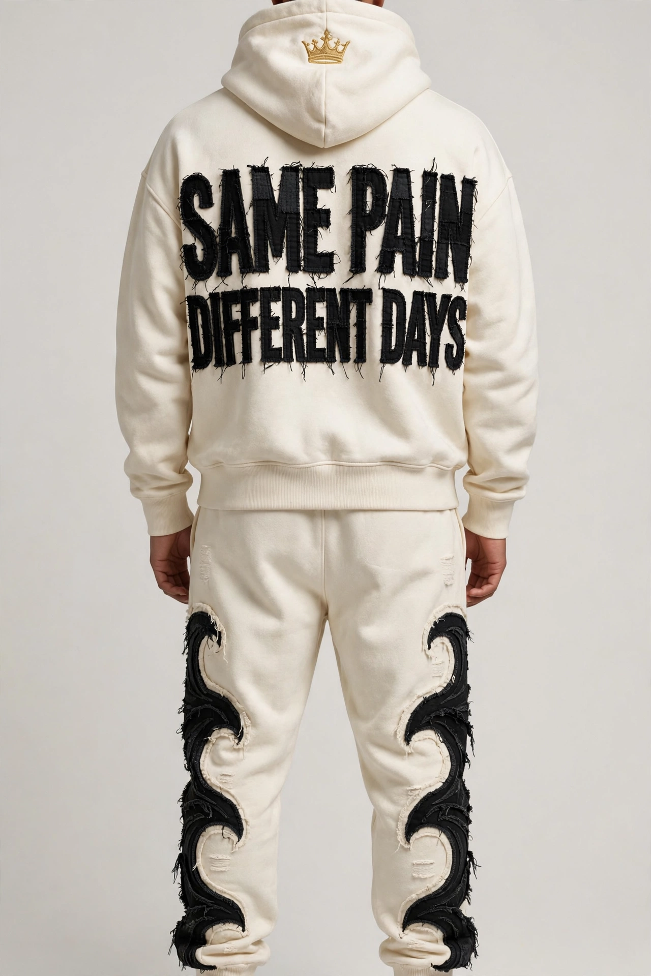 Different Days back-sermon sweatsuit — cream hoodie and sweatpants from the back with SAME PAIN / DIFFERENT DAYS in giant frayed black appliqué and black wave appliqué down both pant legs